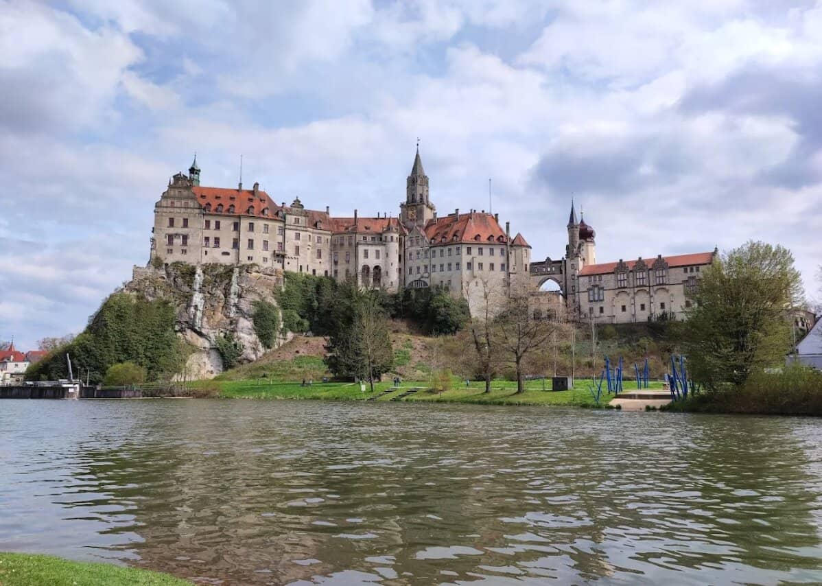 Schloss Sigmaringen vom Donauufer aus mit Wasserspiegelung und bewölktem Himmel